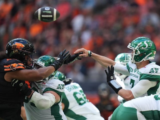 Saskatchewan Roughriders quarterback Trevor Harris, right, passes over B.C. Lions' Tomasi Laulile during the first half of a CFL football game, in Vancouver, on Saturday, July 19, 2025.