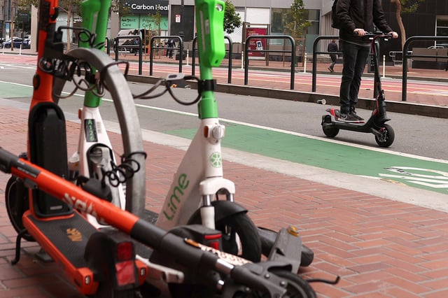 FILE: A man rides an electric scooter by electric scooters parked on Market Street on July 29, 2024, in San Francisco.