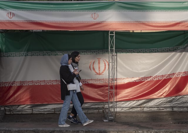 Two young Iranian women walk past the country's flags in northern Tehran, Iran, on June 30, 2025, following the ceasefire between Iran and Israel. (Photo by Morteza Nikoubazl/NurPhoto via Getty Images)