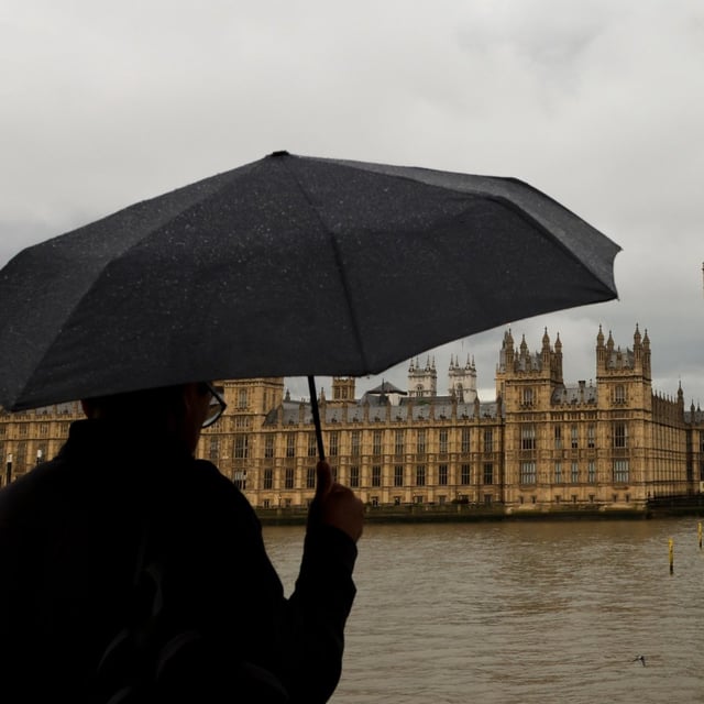 A man under an umbrella looks at the Houses of Parliament and Big Ben in Westminster, London