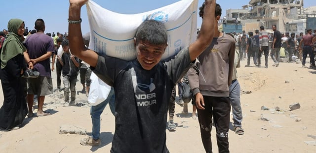 Des personnes se déplacent dans la rue al-Rashid, dans l'ouest de Jabalia, le 22 juillet 2025, après avoir reçu une aide humanitaire dans un centre de distribution situé dans le nord de la bande de Gaza