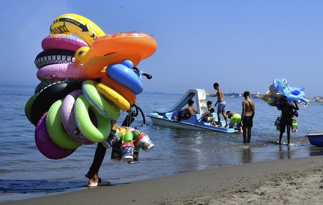 Buoys vendors walk on the beach in Algiers, Friday, July 18, 2025. (AP Photo/Fateh Guidoum)