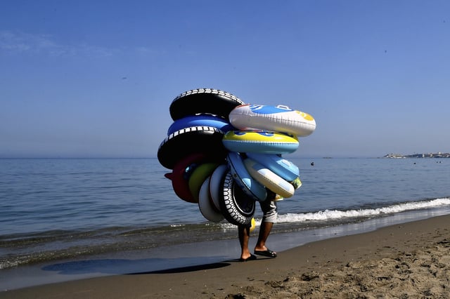 A buoys vendor walks on the beach in Algiers, Friday, July 18, 2025. (AP Photo/Fateh Guidoum)