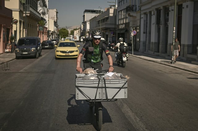 Un coursier à vélo livre du pain aux restaurants et supérettes du centre d'Athènes, pendant une vaugue de chaleur en Grèce, le 8 juillet 2025