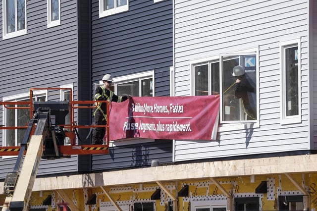 Workers hang a banner prior to a federal government housing announcement in Dartmouth, N.S., on Tuesday, April 2, 2024. THE CANADIAN PRESS/Darren Calabrese