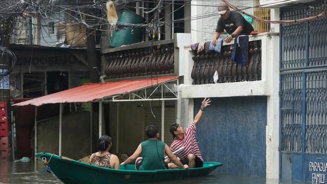 A man catches a plastic container while on a small boat used to ferry residents at a flooded village as intense rains continued in Quezon city, Philippines, on Tuesday. 