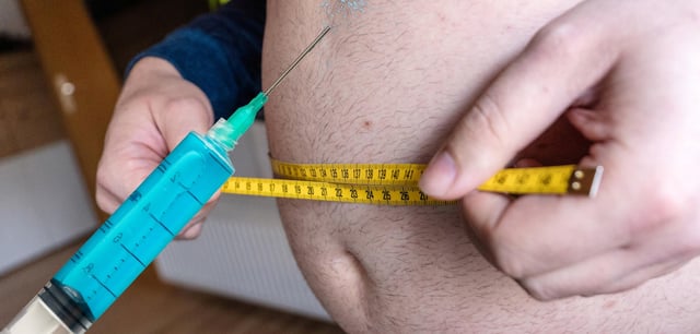Ein Mann hält eine große Spritze, während er mit einem Maßband den Umfang des Bauch misst. Die Fotomontage zeigt ein Anwendungsbeispiel für eine Abnehmspritze
