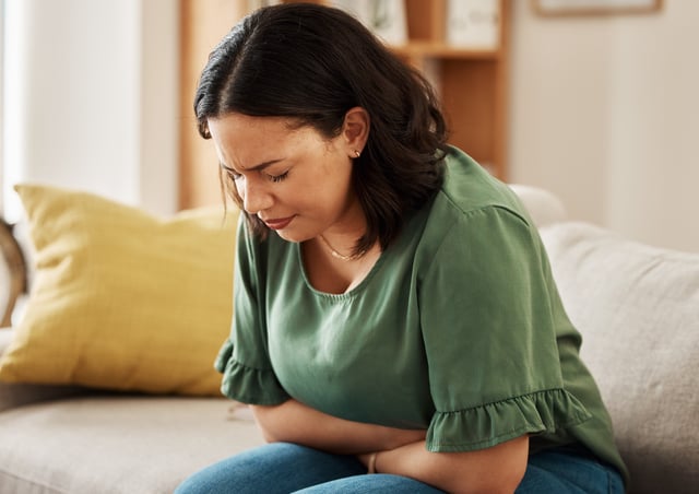 A woman sitting on a sofa experiencing stomach pain and stress.