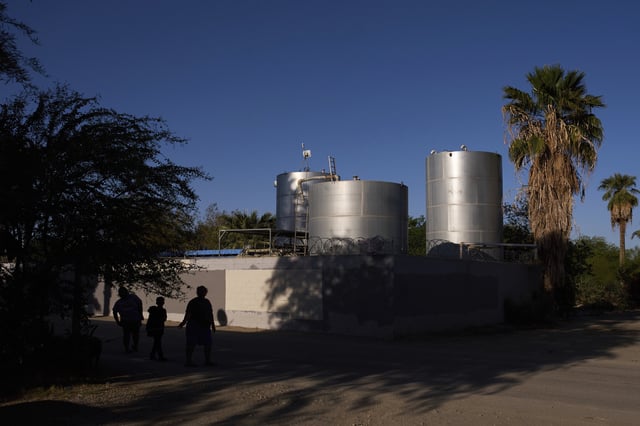 Residents at Oasis Mobile Home Park walk past water tanks in Thermal, Calif., Tuesday, April 15, 2025. (AP Photo/Jae C. Hong)