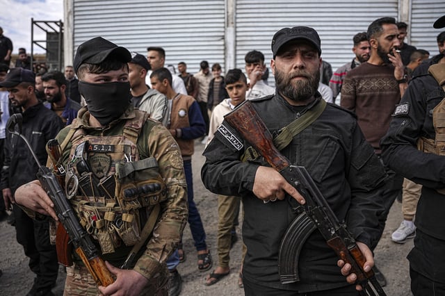 A member of Syrian Democratic Forces (left) and a member of the Syrian Transitional Government&#39;s Public Security Forces stand in the location where a prisoner exchange takes place between the two sides in Aleppo, Syria, on April 3, 2025.