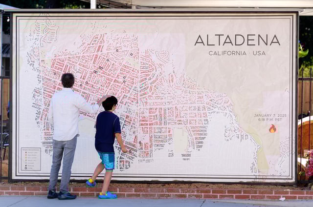 Sam Holtzman and his son Eibu, 9, residents of northwest Altadena, whose house still stands but remains inaccessible due to Eaton Fire contamination in January, look at a map of Altadena fire damage created by Noel McCarthy, a stylized update of Los Angeles County's Eaton Fire damage map, Wednesday, July 9, 2025, in Altadena, Calif. (AP Photo/Chris Pizzello)