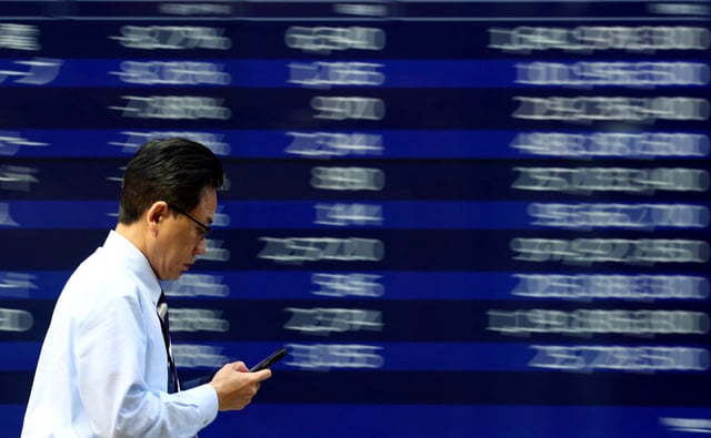 A man walks past an electronic screen displaying stock quotation board in Tokyo, Japan April 15, 2025. REUTERS/Issei Kato/ File Photo