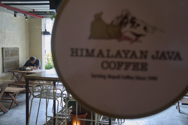 A person checks his mobile phone while drinking coffee at a cafe in Kathmandu, Nepal, Tuesday, June 10, 2025. (AP Photo/Niranjan Shrestha)