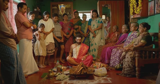 Image shows a Hindu priest seated in front of a ritualistic pyre and people gathered around him to indicate he is conducting a holy pooja.