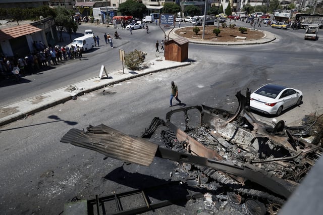 Residents walk past a burned-out military vehicle after last week's sectarian clashes in the Druze-majority town of Sweida, Syria, on Friday, July 25, 2025. (AP Photo/Omar Sanadiki)