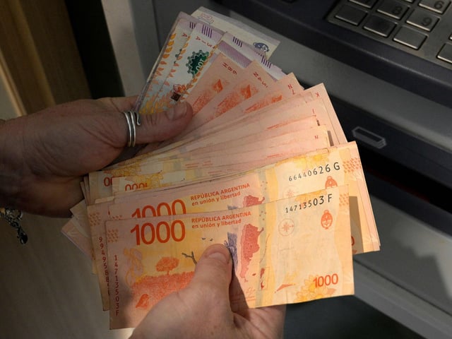 (FILES) A woman withdraws Argentine pesos from an ATM machine at a bank in Buenos Aires on November 4, 2021. Argentine monetary authorities on August 14, 2023, devalued the peso by around 20 percent in anticipation of a mtsunami." (Photo by Juan MABROMATA / AFP)  pesos billetes de mil cajero automatico