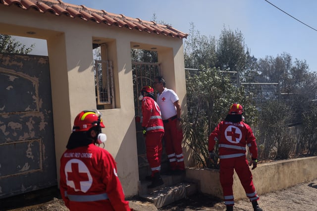 Hellenic Red Cross volunteers look for locals inside houses as a wildfire burns in the village of Thymari, near Athens, Greece, June 26, 2025. REUTERS/Stelios Misinas