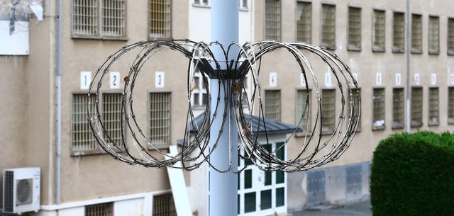 Stacheldraht und vergitterte Fenster im Sicherheitsbereich einer Justizvollzugsanstalt