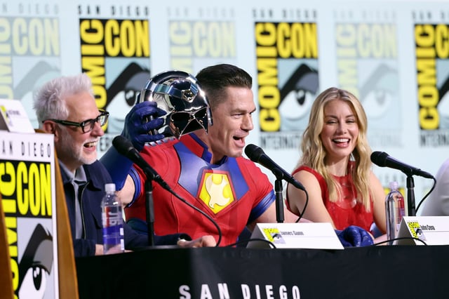 John Cena (center) does a "You can't see me" gag as James Gunn and Jennifer Holland laugh during the "Peacemaker" panel at Comic-Con.