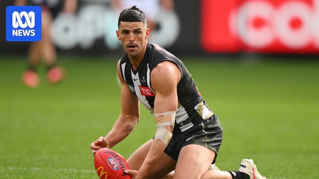 AFL player stoops to pick up a ball.