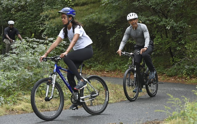 FILE - President Barack Obama follows his daughter Malia Obama as they rides bikes in West Tisbury, Mass., on Martha's Vineyard, Aug. 22, 2015, during the Obamas annual vacation. (AP Photo/Susan Walsh, File)