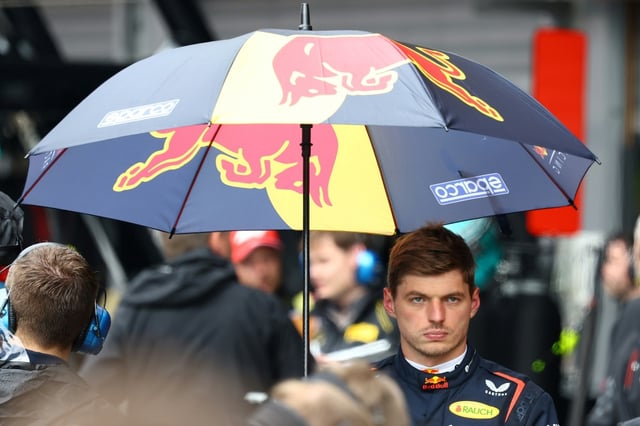 Max Verstappen takes refuge under an umbrella as rain delays Belgian Grand Prix start