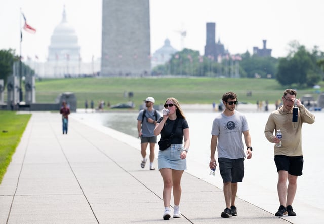 Tourists drink water as they walk along the National Mall near the Washington Monument in Washington, DC, July 25, 2025, as a heat dome sits over the region leading to extremely high temperatures.