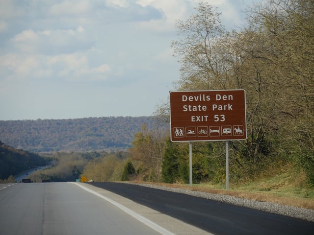 A roadside sign with exit directions to Devils Den State Park at Interstate 49, Arkansas.