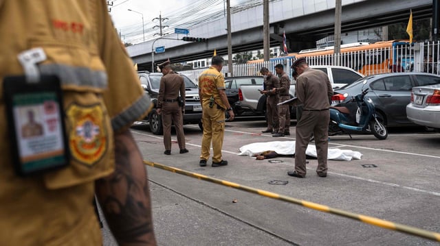 Polizisten stehen neben einer abgedeckten Leiche in Bangkok.
