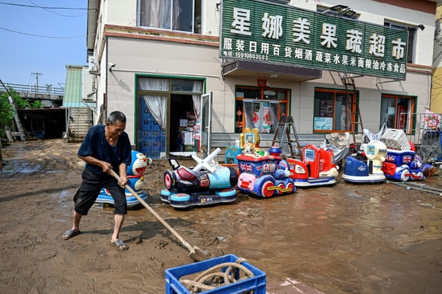Un homme âgé déblaye la boue devant un marché inondé après de fortes pluies dans le village de Taishitun, dans le district de Miyun, à la périphérie de Pékin, le 28 juillet 2025