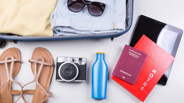 Ein gepackter Koffer neben dem ein Reisepass liegt.