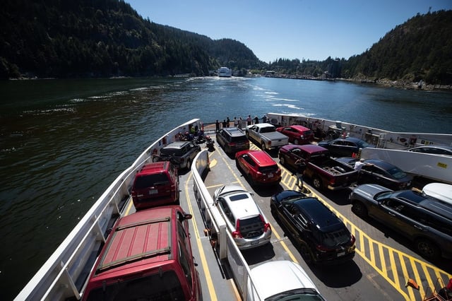 People stand on the vehicle deck as others sit in their cars on the BC Ferries vessel Queen of Capilano as it arrives at Horseshoe Bay, B.C., after sailing from Bowen Island, on Tuesday, July 19, 2022. 