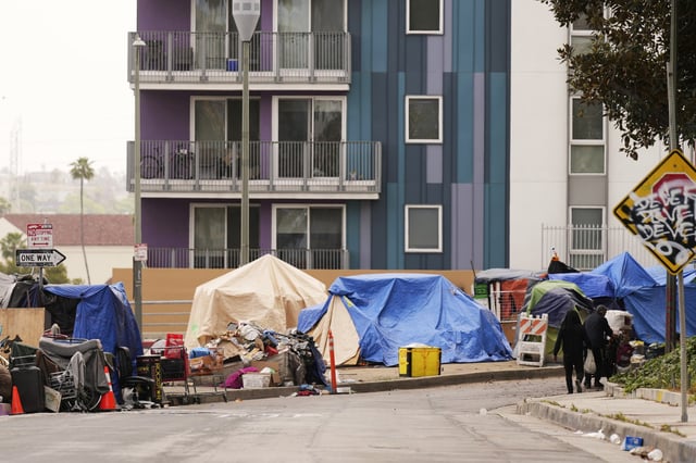 Pedestrians walk past tents set up along a freeway in a homeless encampment, in Los Angeles, on May 12, 2025.