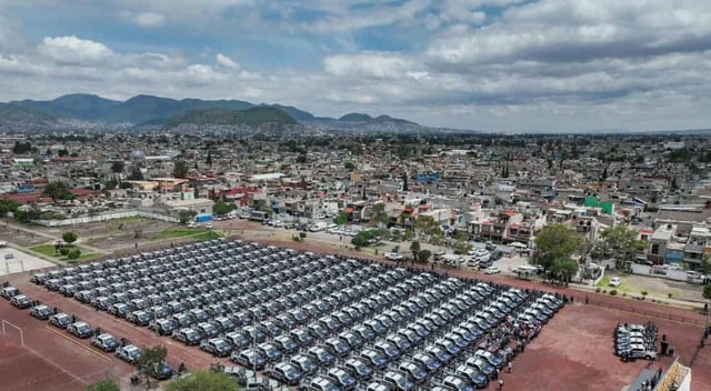 Imagen aérea de un campo deportivo en Ecatepec con filas perfectamente alineadas de más de 450 patrullas y motopatrullas, durante un evento oficial encabezado por la gobernadora Delfina Gómez, con presencia de autoridades civiles y militares, en el contexto de una estrategia de seguridad pública