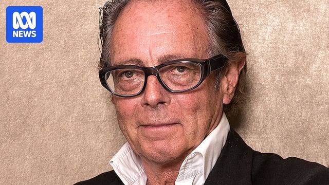 A close up photo of an older man with glasses and a receding hairline