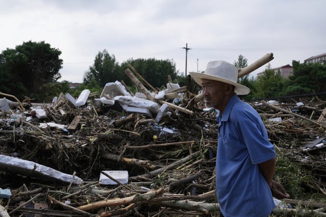 A man looking at a damaged road littered with broken tree branches after a heavy rains in Taishitun Town, Miyun district on the outskirts of Beijing, China, Monday, July 28, 2025. (AP Photo/Mahesh Kumar A.)