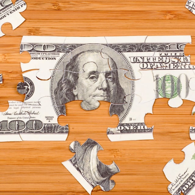 Puzzle of a hundred-dollar bill on a wooden background.