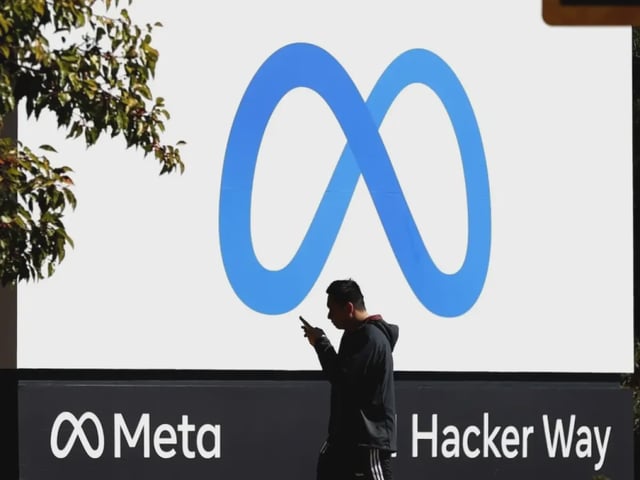 A man walking past a Meta sign outside an office location.