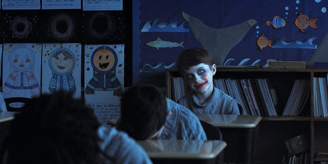 Alex Lilly at a classroom desk with clown makeup and an unnerving smile in Weapons
