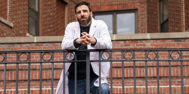 Zachary Quinto as Dr. Oliver Wolf leaning on a railing outside of the hospital in Brilliant Minds.