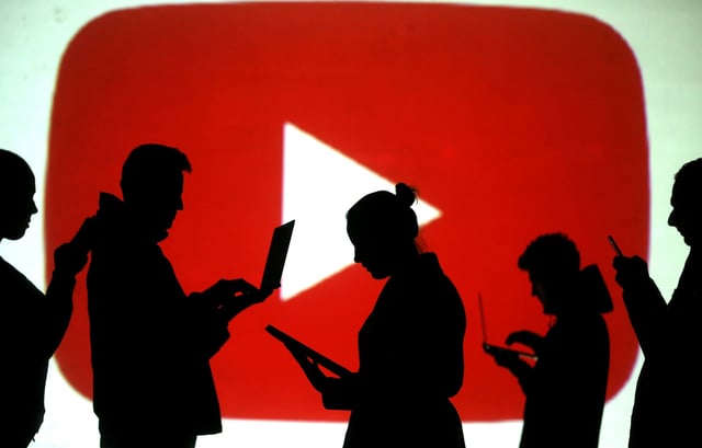 Silhouettes of laptop and mobile device users are seen next to a screen projection of Youtube logo in this picture illustration taken March 28, 2018. REUTERS/Dado Ruvic/Illustration