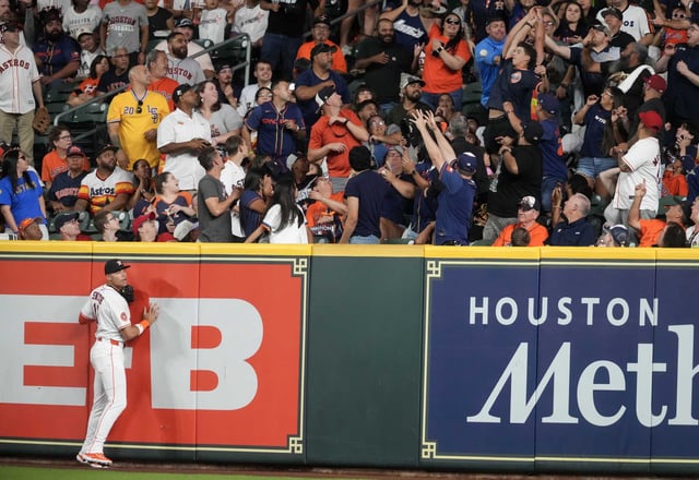Houston Astros right fielder Cam Smith (11) hits the outfield wall as fans reach for Washington National Luis García Jr.’s  two-run home run during the third inning of an MLB baseball game in Houston, Tuesday, July 29, 2025.