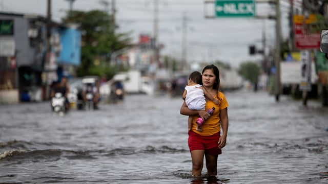 A woman carrying a baby wades through a flooded area in Manila North Road following heavy rains brought by Typhoon Co-may in Minalin, Pampanga, Philippines. The storm is now expected to head to Shanghai.