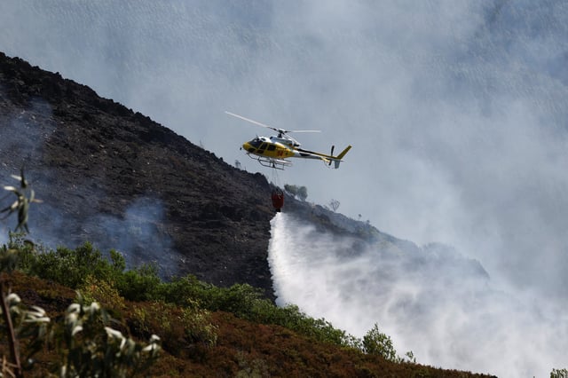 A helicopter unloads water as efforts to battle a wildfire in the Arouca region continue, Portugal, July 30, 2025. REUTERS/Violeta Santos Moura