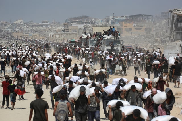 Palestinians walk carrying sacks of flour near Jabalia, in the northern Gaza Strip, on July 27, 2025, after trucks carrying humanitarian aid entered into northern Gaza coming from the Zikim border crossing. Jordanian and Emirati planes dropped food into Gaza on July 27, as Israel began a limited "tactical pause" in military operations to allow the UN and aid agencies to tackle a deepening hunger crisis. (Photo by BASHAR TALEB/AFP via Getty Images)