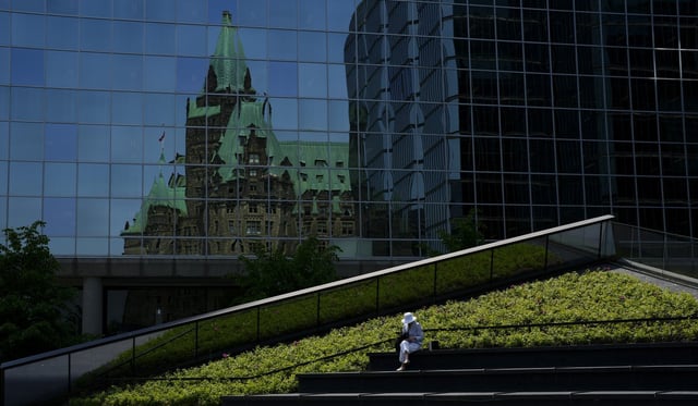 A person sits outside the Bank of Canada in Ottawa on Wednesday, June 4, 2025. The Confederation Building on Parliament Hill is reflected in the windows behind. THE CANADIAN PRESS/Sean Kilpatrick