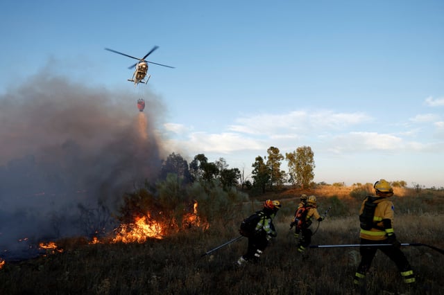 Forest rangers walk away from a helicopter waterdrop to put out a wildfire on the outskirts of Valmojado, Spain, July 17, 2025. REUTERS/Susana Vera/File Photo