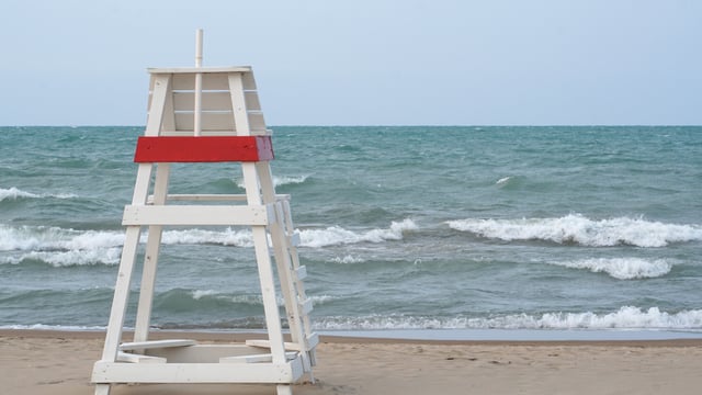 A stock photo shows an empty lifeguard chair facing choppy waters on Lake Michigan.