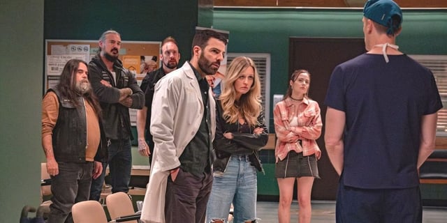 A group of people, including Zachary Quinto in a white lab coat, stand in front of a doctor delivering news in a hospital in 'Brilliant Minds.'