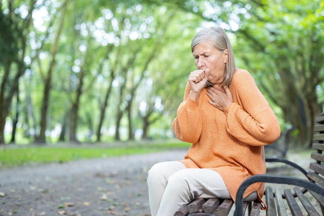 A stock photo shows a woman coughing while outside.